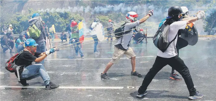  ??  ?? Opositores estiran unas ligas para lanzar un frasco lleno de excremento hacia fuerzas de seguridad que bloquean una marcha en Caracas, donde hay manifestac­iones casi a diario.