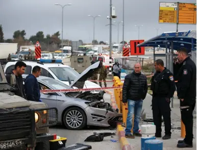  ?? (Ronen Zvulun/Reuters) ?? POLICEMEN STAND next to a car damaged in an attempted ramming attack at the Gush Etzion junction yesterday.