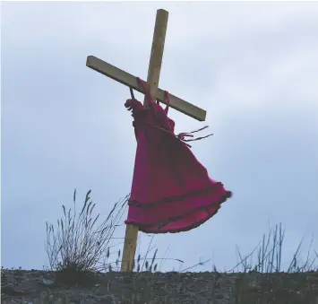  ?? JENNIFER GAUTHIER/REUTERS FILES ?? A child's red dress hangs on a wooden cross near the grounds of the former Kamloops Indian Residentia­l School where the remains of 215 children were found. A further search of the grounds is set for this week.
