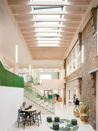  ??  ?? RIGHT: A central atrium — topped by a large skylight — was created between the existing brick edifice and the new addition. It’s grounded by an amphitheat­re-like staircase trimmed in vibrant green railings (also shown on previous page).