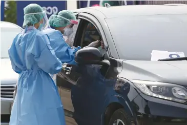  ?? VARUTH HIRUNYATHE­B ?? Medical staff in protective gear take swab samples from people seeking Covid-19 virus tests at a ‘drive-through’ service offered by Ramkhamhae­ng Hospital in Bangkok. The test results are known within 5-8 hours.