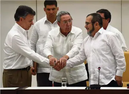  ?? Luis Acosta /AFP / Getty Images ?? Colombian President Juan Manuel Santos, left, and the head of the FARC guerrilla Timoleon Jimenez greet each other with help from Cuban President Raul Castro during a meeting in Havana.