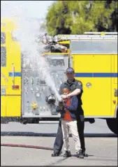  ??  ?? Clark County Fire Department fireman Daniel Mawhinney assists Tyriq Beacham, 12, with opening a hose for children to play in water during Saturday’s event.