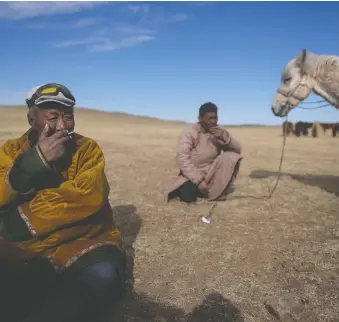  ?? MANISH SWARUP/THE ASSOCIATED PRESS ?? Herder Lkhaebum, 71, and his assistant take a cigarette break as they relocate their livestock in southeast Mongolia.