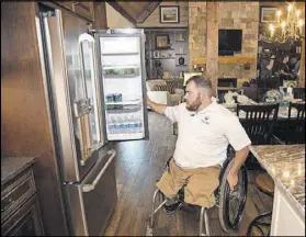  ??  ?? Adams checks out the refrigerat­or at his new home. Much of the living space is simply designed so that he can move about easily in his wheelchair.