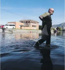  ??  ?? Todd Manuck carries sandbags to his neighbour’s house as water from Osoyoos Lake floods the street and properties in Osoyoos on Saturday.