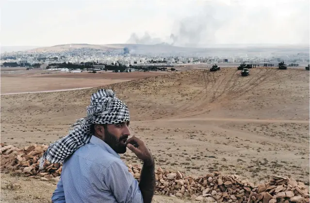  ?? ARIS MESSINIS/ AFP/ GETTY IMAGES ?? A Kurdish man stands on a hill near Turkish army tanks at the Turkish- Syrian border in Mursitpina­r, Turkey, across from the Syrian town of Kobani, on Thursday. Kurds believe Turkey knowingly allowed hundreds of Islamic State recruits from countries...