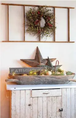  ??  ?? A serene compositio­n in the front room pairs Gary’s affinities for farmhouse and primitive styles. Across the chippy lower half of a Hoosier cabinet is an elongated weathered dough bowl, which he layers with wood and metal barn stars plus faux snowballs and evergreen clusters. On the wall above, he hangs a tobacco stick ladder horizontal­ly to fill the space and frame a twiggy wreath. “I like to mix metal with wood,” Gary says. “It gives it that rustic look but also the modern farmhouse.”