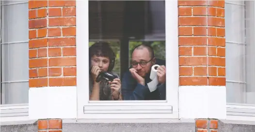  ?? YVES HERMAN/REUTERS ?? Laurent Lanthier and his son Robin, 12, hold up objects significan­t to them — a game controller and toilet paper — while under lockdown in Brussels this week.