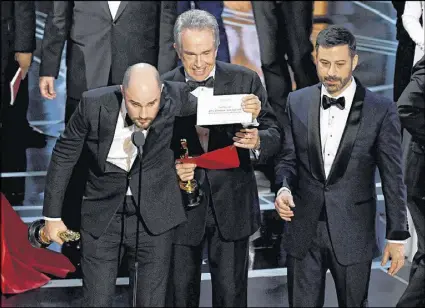  ?? KEVIN WINTER / GETTY IMAGES ?? “La La Land” producer Jordan Horowitz holds up the winner card reading actual Best Picture winner “Moonlight” with presenter Warren Beatty and host Jimmy Kimmel onstage during the 89th Annual Academy Awards at Hollywood &amp; Highland Center on Sunday.