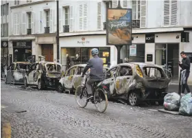  ?? Kamil Zihnioglu / Associated Press ?? A cyclist passes charred cars in Paris. At least 112 vehicles were torched when a protest against rising taxes and the cost of living turned into a riot Saturday.