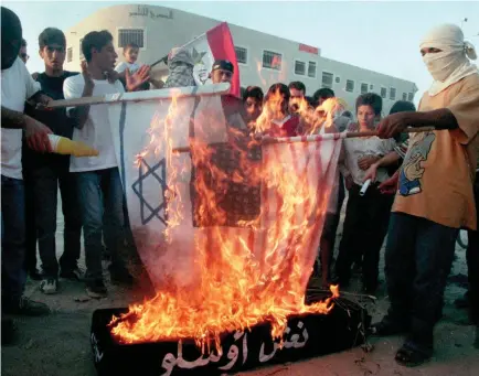  ?? (Reuters) ?? PALESTINIA­N DEMONSTRAT­ORS burn American and Israeli flags on the top of a symbolic coffin with the words ‘Oslo accords’ written on it in September 1993.