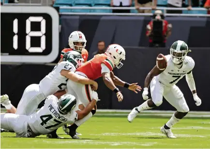  ?? DAVID SANTIAGO dsantiago@miamiheral­d.com ?? Hurricanes quarterbac­k D’Eriq King fumbles against the defense from the Spartans’ Cal Haladay (27), Jeff Pietrowski (47) and Michael Dowell (7) in the first quarter on Saturday at Hard Rock Stadium. King fumbled twice and was intercepte­d twice in the loss to Michigan State.