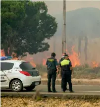  ?? AP ?? Police and Civil Guards look towards a forest fire near Mazagon in southern Spain. —