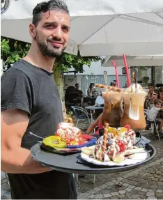  ??  ?? Sergio verwöhnt in Krumbach seine Gäste mit leckeren Eisbechern. In den Eisdielen herrscht bei der Hitze Hochkonjun­ktur.