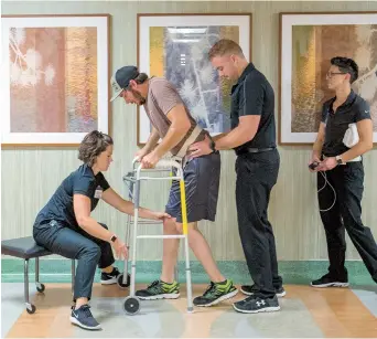  ??  ?? Jered Chinnock walks down a clinic hallway with his therapy team at the Mayo Clinic. Chinnock, paralyzed since 2013, is taking steps again thanks to an electrical implant that zaps his injured spine, along with months of intense rehab. — IC