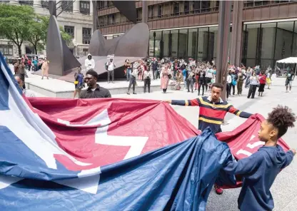  ?? ANTHONY VAZQUEZ/SUN-TIMES ?? Tau Kennebrew, Tendaji Andrew-Hutchinson and Asha Andrew-Hutchinson help unfurl the flag during the Juneteenth flag raising at Daley Plaza on Monday.