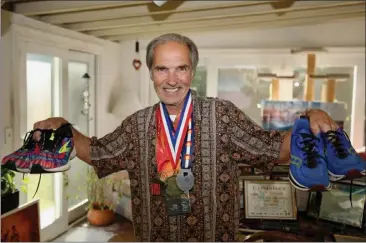  ?? PHOTOS BY HOWARD FRESHMAN ?? David Bergeron holds running shoes in each hand and wears medals he won from the many marathons he has run. Bergeron, 68, of Long Beach has set out to run a marathon in all 50states. He finished his goal, over 39years, with a run in Hawaii.