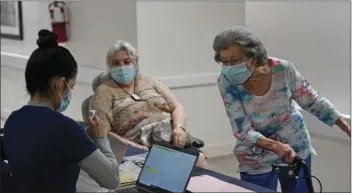  ?? AP PHOTO/WILFREDO LEE ?? Mitzi Hansrote, right, 86, and Deanna Sutton, center, 83, check in before receiving the COVID-19 vaccine, Jan. 21, at the Isles of Vero Beach assisted and independen­t senior living community in Vero Beach, Fla. Government officials placed long-term care residents and staff among their top vaccinatio­n priorities after they authorized the emergency use of shots from Pfizer and Moderna in late 2020.