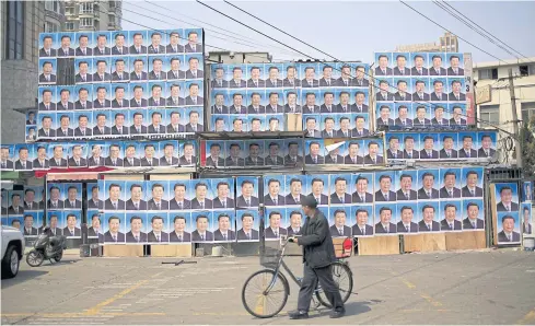  ?? REUTERS ?? A man with a bicycle walks past a building covered in hundreds of posters of Chinese President Xi Jinping in Shanghai, China. Fifty years after the Cultural Revolution launched by Mao Zedong, Mr Xi has attempted to secure Mao-style control.