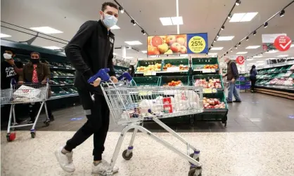 ?? Photograph: Peter Cziborra/Reuters ?? A man wearing a face mask pushes a shopping cart at a Tesco supermarke­t