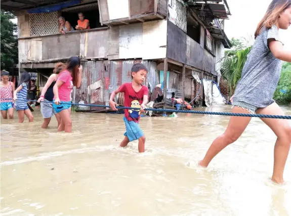  ?? JOY TORREJOS ?? Residents of Barangay Paknaan in Mandaue City hold on to a rope as they cross a flooded street following continuous rains on New Year's Day as tropical depression Agaton passed by southern Cebu.