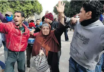  ?? KHALIL HAMRA/THE ASSOCIATED PRESS ?? Egyptians help an elderly woman as she tries to cross the street during clashes between protesters and riot police near Cairo’s Tahrir Square on Sunday. Rioters are protesting the death sentences a court handed to 21 soccer rioters.