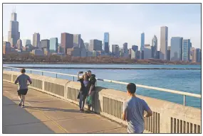  ?? (File Photo/AP/Shafkat Anowar) ?? A couple poses for a selfie March 9 as joggers pass by along Lake Michigan at Lakefront Trail in Chicago.