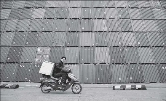  ?? REUTERS ?? A man rides his motorcycle past shipping containers at the Port of Shanghai.