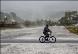  ?? LUCANUS OLLIVIERRE — THE ASSOCIATED PRESS ?? A man rides his bicycle past fields covered with volcanic ash a day after the La Soufriere volcano erupted, in Kingstown, on the eastern Caribbean island of St. Vincent, on Saturday.