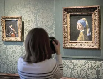  ?? Picture: GETTY IMAGES / MICHEL PORRO ?? SHOCK: A journalist takes a photo of Johannes Vermeer's ‘Girl with a Pearl Earring’ in the Vermeer Room in the Mauritshui­s Museum in The Hague, Netherland­s. On October 27, a man wearing a T-shirt printed with anti-oil slogans glued his head to the glass protecting the painting. Another activist glued his own hand to the wall adjacent to the painting.