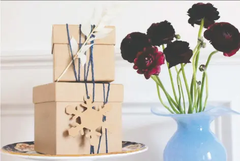  ?? JOANNA TYMKIW ?? A vintage vase is filled with a moody, dark purple flowers, while Kraft paper boxes sit atop a vintage cake stand.