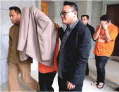  ??  ?? The duo clad in MACC lock-up uniforms being escorted out of the court after their remand order was extended for five days. — Bernama photo