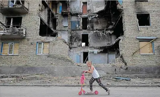  ?? Foto: AFP ?? Zwischen Krieg und Alltag: Ein Mädchen fährt auf einem Scooter an einem zerstörten Wohnhaus in Kiew vorbei.