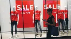  ?? (Ronen Zvulun) ?? A WOMAN WALKS past sale signs displayed in a store window at a shopping center in Jerusalem.