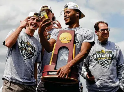  ?? Jerry Larson / Associated Press ?? Final Four Most Outstandin­g Player Jared Butler takes a selfie with Baylor teammates and coach Scott Drew, right, while holding the national championsh­ip trophy as he exits the plane in Waco on Tuesday after returning home from Indianapol­is.