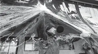  ?? Karen Warren / Staff photograph­er ?? Hector Castro with Gulf Coast Canvas Awnings helps install a clear plastic patio enclosure for a restaurant Monday in the Heights as a gust of wind hits.