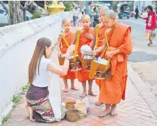  ?? ?? A woman offers food and alms to Buddhist monks in the early morning in front of a pagoda.