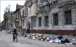  ?? THE ASSOCIATED PRESS ?? A woman rides a bike past a building damaged during fighting in Mariupol in eastern Ukraine on Wednesday.