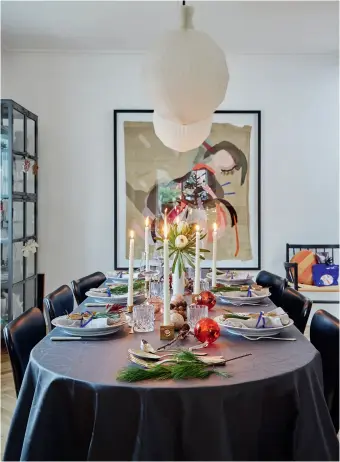  ??  ?? Bordet er daekket til julemiddag med snoede lys fra Broste Copenhagen, tallerkene­r fra Royal Copenhagen, servietter fra Georg Jensen Damask og sølvbestik, der er et arvestykke fra Franks farmor. Det store vaerk på vaeggen er lavet af Pernille Egeskov.
Juletraeet er fyldt med minder. Kagemanden er 15-årige Augustas, filtkuglen har Frida på 11 år lavet, og nissen har Frank haft, siden han var dreng.