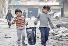  ?? — AFP ?? Syrian children walk carrying a bag along a damaged street in Aleppo’s Tareeq al Bab neighbourh­ood, a month after government forces retook the northern Syrian city from rebel fighters.