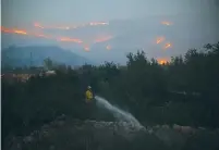  ?? (Ammar Awad/Reuters) ?? A FIREMAN SPRAYS WATER near a home in Nataf as flames burn on the hills west of Jerusalem last month.