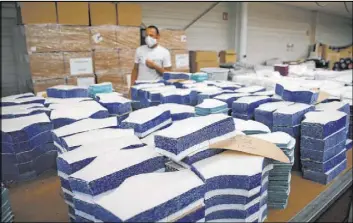  ?? Francois Mori The Associated Press ?? A worker walks by fabric cut for face masks at Chanteclai­r Hosiery, a knitwear clothing manufactur­er, in Saint Pouange, east of Paris. Several companies have a mask surplus.