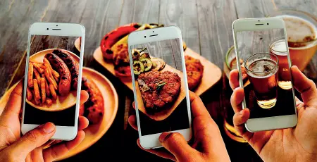  ??  ?? A tavola Ormai si impugna più spesso lo smartphone che la forchetta per poter immortalar­e il cibo che si mangia o i commensali con cui si mangia