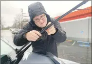  ?? (NWA Democrat-Gazette/Andy Shupe) ?? Ben Walsh (above photo) changes the windshield wiper blades Monday on his car in the rain outside AutoZone at College Avenue and Lafayette Street in Fayettevil­le. A Fayettevil­le Police vehicle (left photo) blocks the northbound lanes Monday of School Avenue near Lester Street after a large cedar tree fell onto the roadway. High winds Monday morning were followed by rain for much of the day with snow expected overnight. Visit nwaonline. com/photo for today’s photo gallery.