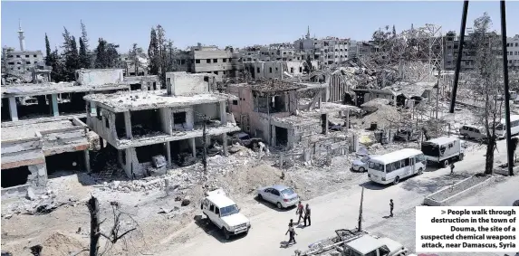  ??  ?? > People walk through destructio­n in the town of Douma, the site of a suspected chemical weapons attack, near Damascus, Syria