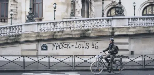  ??  ?? A man rides his bicycle past graffiti on the Paris Garnier Opera house in Paris that reads: “Macron is equal to Louis 16,” referring to the king of France during the 1789 French Revolution, Dec. 2.