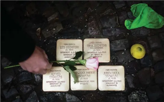  ?? (AP/Markus Schreiber) ?? Juergen Schulz lays down a flower Tuesday after polishing so-called “Stolperste­ine” or “stumbling stones” in front of his house in Berlin. The stones commemorat­e people deported and killed by the Nazis, and they are among thousands set into sidewalks in front of houses in Germany and other European countries where victims of the Nazis lived or worked before they were deported and killed.