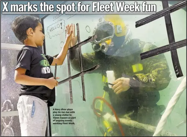  ??  ?? A Navy diver plays play tic-tac-toe with a young visitor to Times Square as part of ongoing events marking Fleet Week.