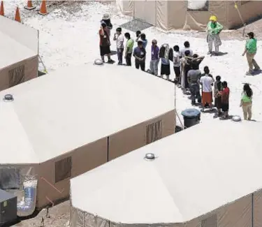  ?? GETTY ?? Workers and children separated from their families (above) line up at a tent encampment recently built near the Tornillo Port in Tornillo, Texas. A protester (below) holds a sign outside a closed gate of a camp.